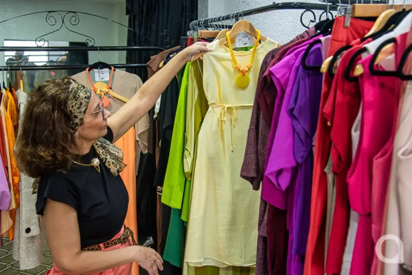 Mulher branca em pé segurando um vestido na cor amarela. Ela é dona de uma loja pertinho de casa.