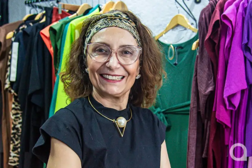 Mulher branca usando óculos e sorrindo. Ela é dona de uma loja pertinho de casa.