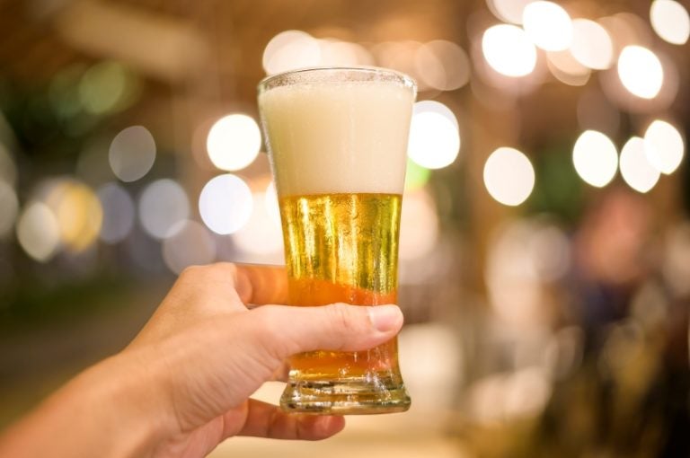 Close Up Of Hand Holding A Glass Of Beer To Celebrate At Restaurant.