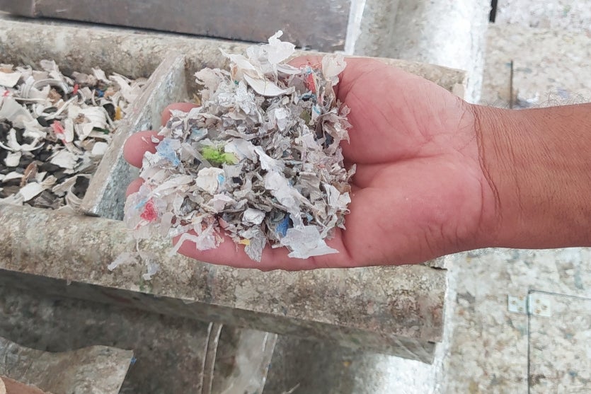 Mão de um homem branco segurando as caixinhas de leite trituradas