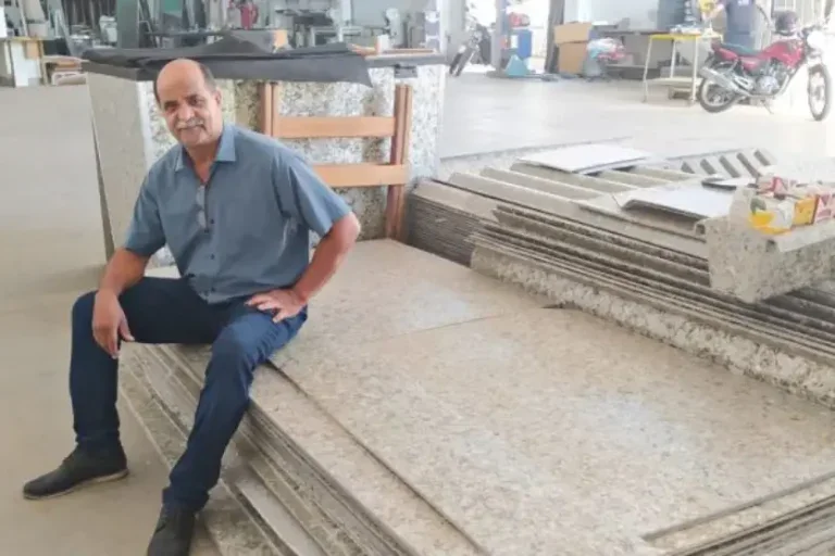 Homem branco está sentado sobre uma pilha de placas feitas com as caixinhas de leite.