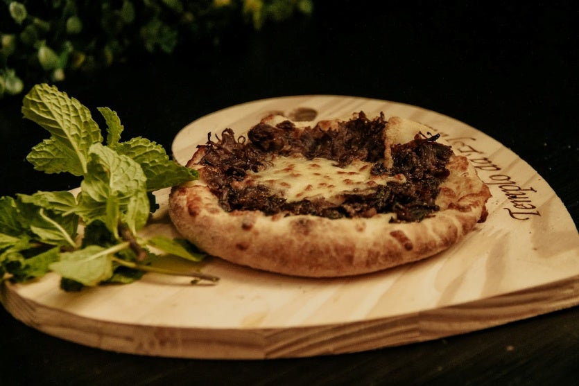 foto de uma esfiha de carne em cima de uma tábua de madeira com ramos verdes enfeitando.
