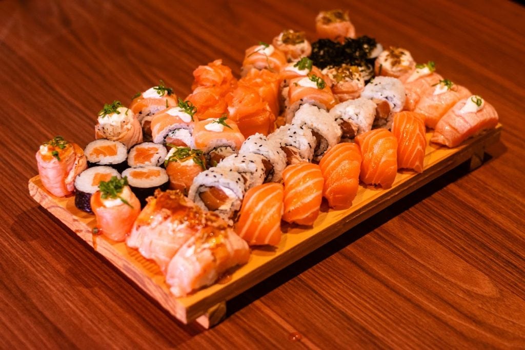 Tábua de madeira com comida oriental sobre ela em cima de uma mesa.