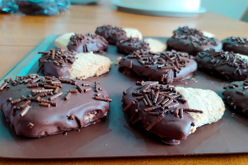 bolachas sem glúten e sem lactose cobertas com chocolate e granulado de chocolate em cima de uma tábua marrom