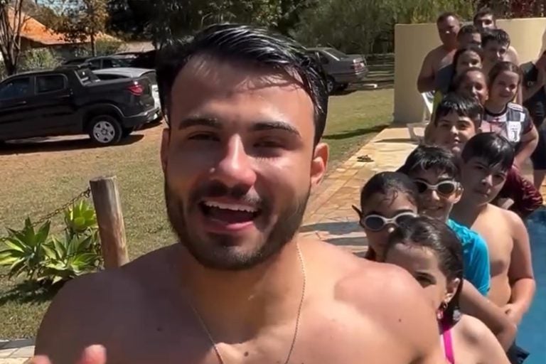 Padre Kenny sem camisa em uma fila à frente de crianças, preste a pular na piscina