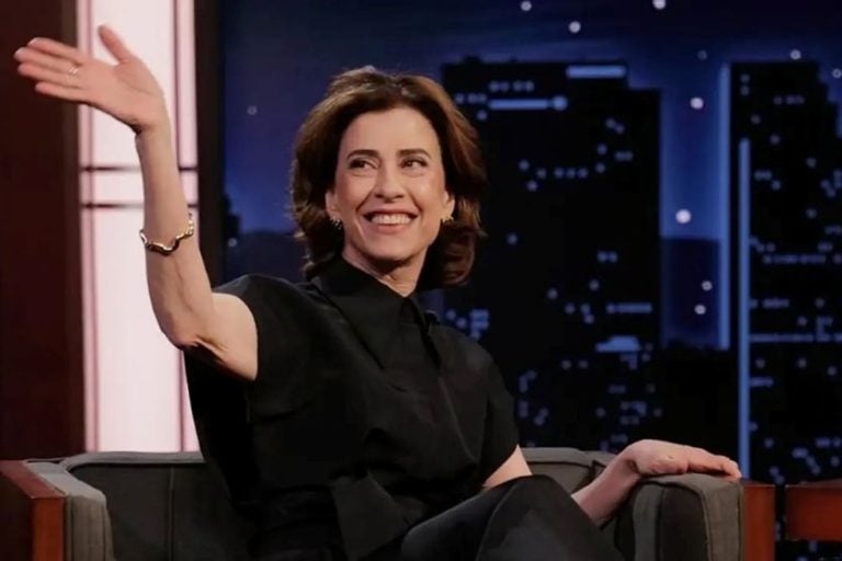 Atriz Fernanda Torres acenando para o público sentada em um sofá durante uma entrevista