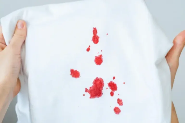Mãos de uma pessoa branca segurando uma roupa branca com manchas de sangue