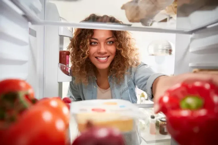 Mulher negra sorrindo pegando um alimento dentro da geladeira