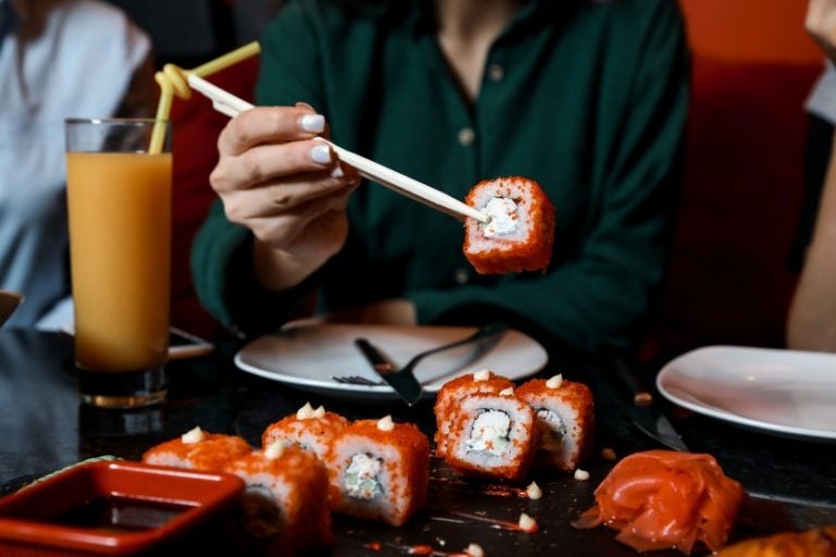 Mão segura talher com comida oriental em uma mesa