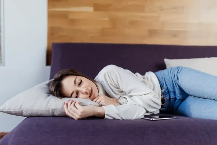 Mulher branca de cabelo castanho dormindo de lado em um sofá roxo
