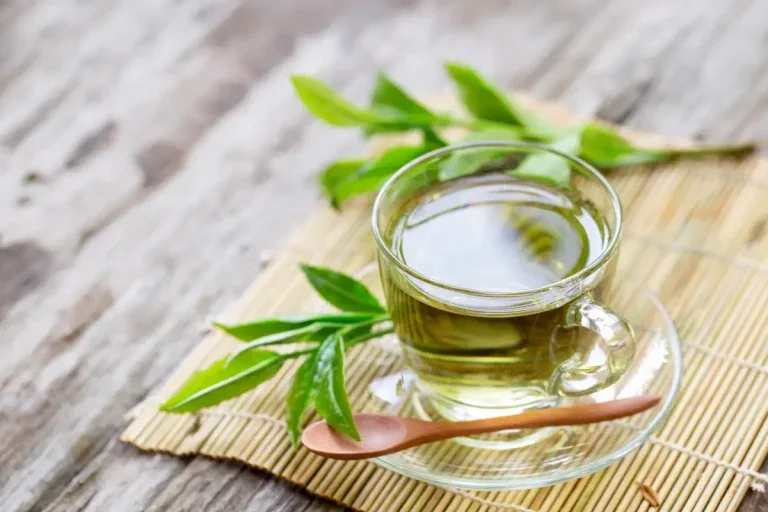 Xícara transparente com chá verde em cima de uma mesa de madeira.