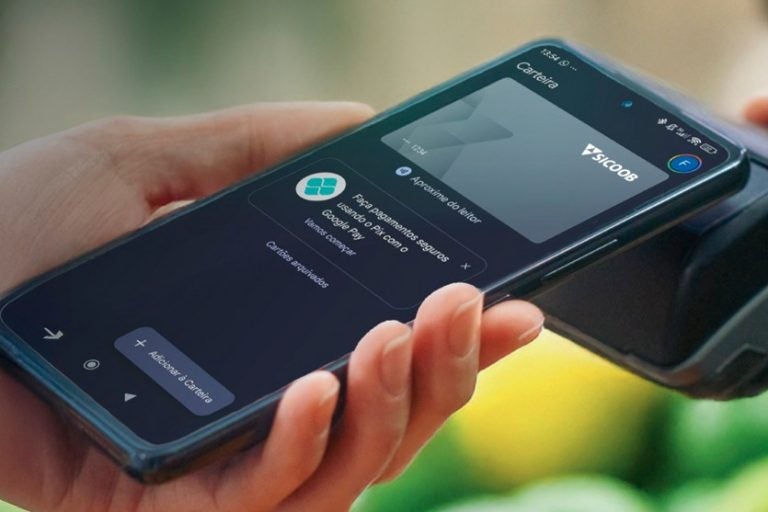 Sicoob passa a oferecer Google Pay. Na foto, uma mão segurando um celular com a tela no Sicoob e a opção de Google Pay.