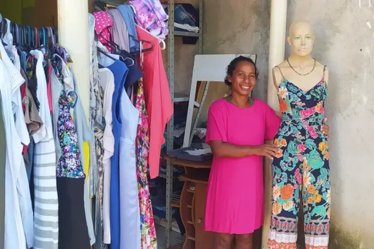 Mlher negra de vestido rosa ao lado de um manequim com uma roupa estapada. Foto para ilustrar a matéria sobre mulher monta brechó em casa.