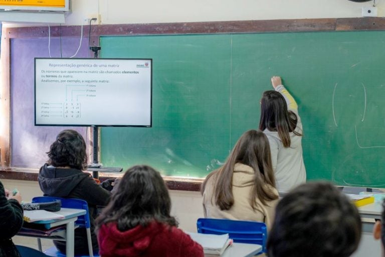 Convocação de professores no Paraná. Na foto, uma sala de aula com uma professora escrevendo na lousa.