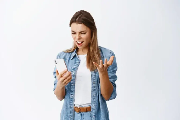 Mulher branca em pé segurando um celular e irritada. Foto para ilustrar a matéria sobre ligações indesejadas.