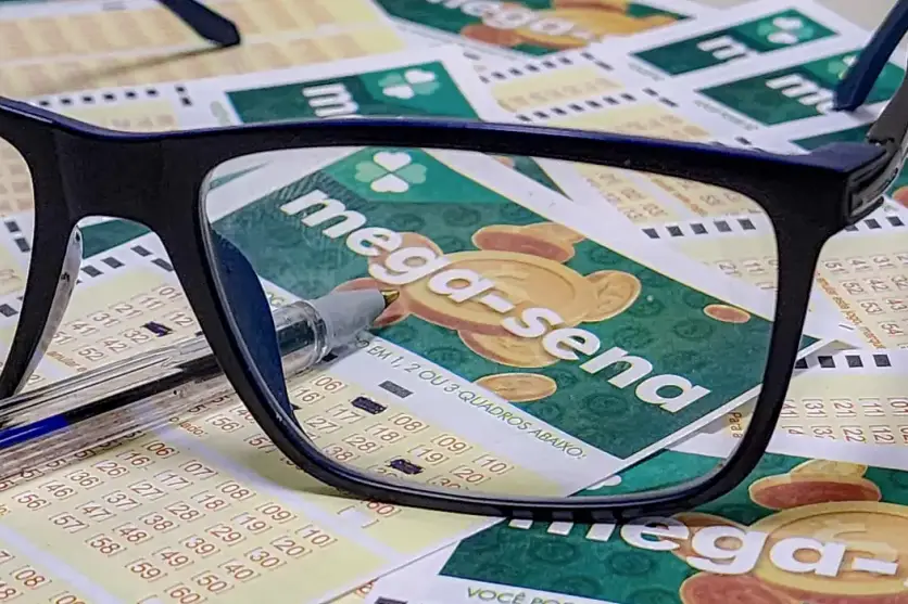 Na foto, um óculos sobre vários bilhetes da Mega-Sena, para ilustrar a matéria do prêmio acumulado em R$ 115 milhões.