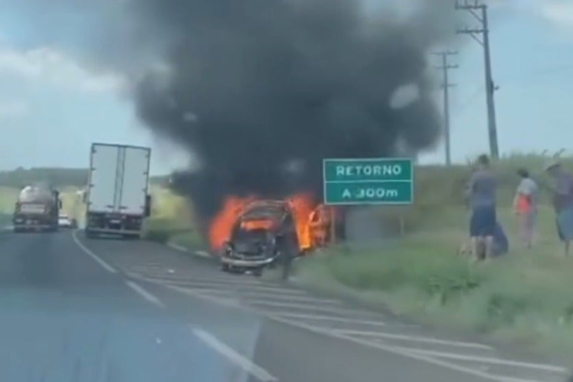Fusca que explodiu em chamas às margens da BR-376 enquanto testemunhas socorrem a vítima próximo ao veículo