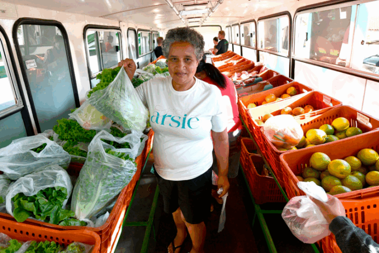 Mulher segurando uma sacola com verduras pesadas na feirinha itinerante de Umuarama.