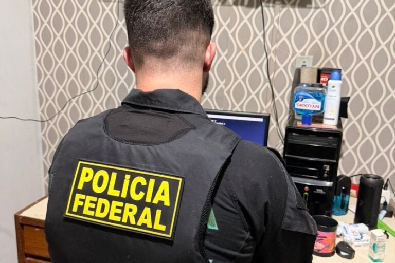 Policial Federal sentado em frente a um notebook durante o cumprimento do mandado que resultou no homem preso em Umuarama durante operação contra abuso infantil.