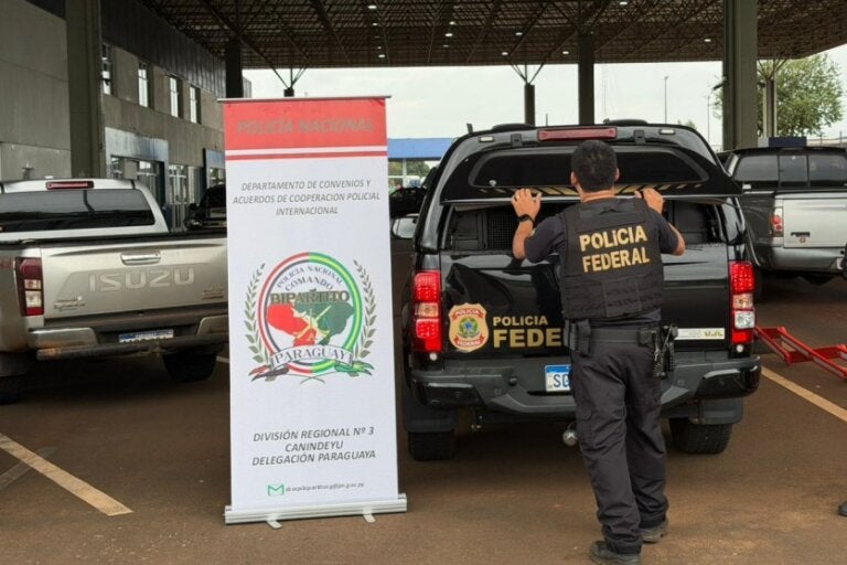 Policial federal próximo a uma viatura e um cartaz para ilustrar a matéria de um brasileiro detido no Paraguai.