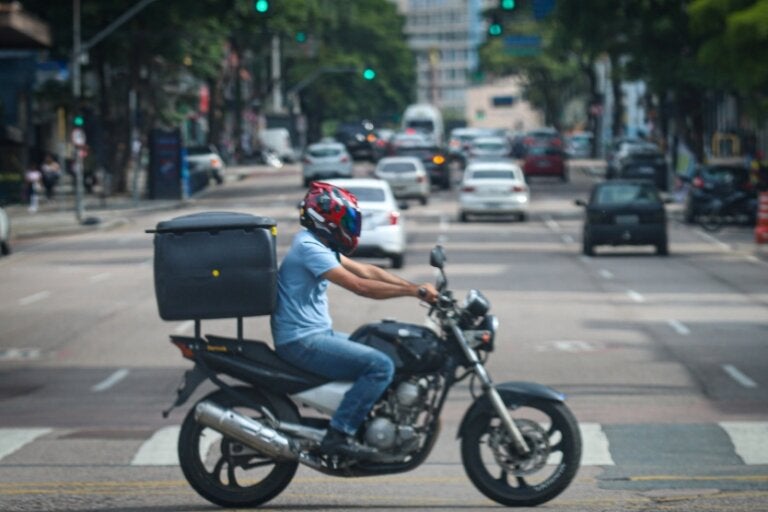 Foto de um motociclista com uma moto equipada com baú de delivery.