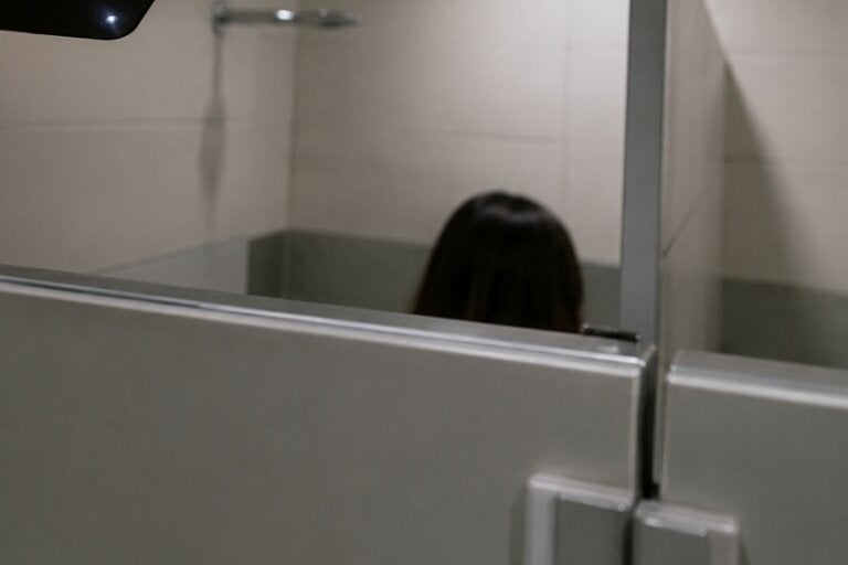 Câmera próxima a uma mulher em uma cabine de banheiro.