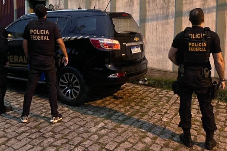 Foto de agentes da Polícia Federal próximo a uma viatura.