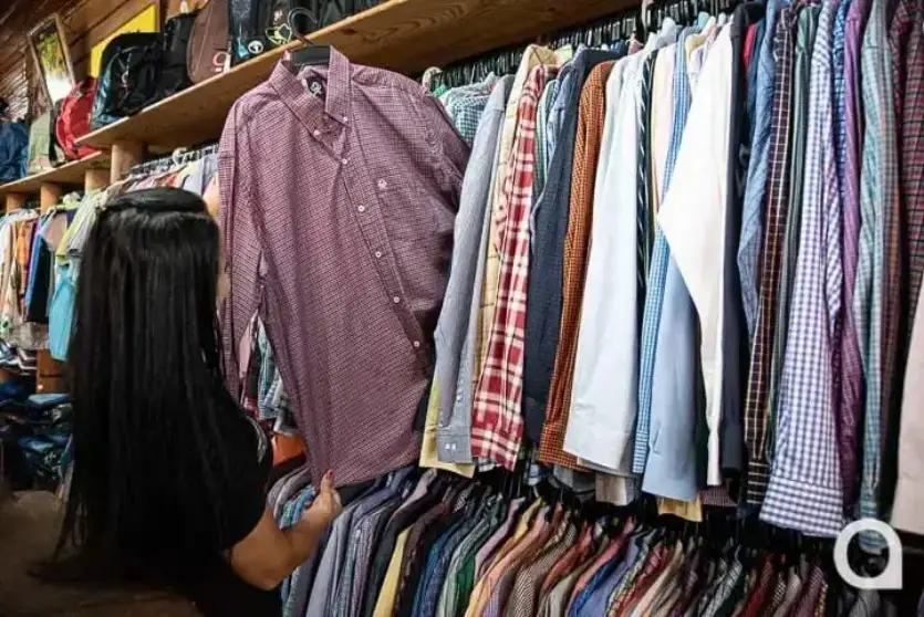 Pessoa escolhendo camisas masculinas em uma loja de roupas em Umuarama.