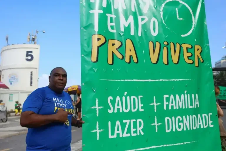 Trabalhador ao lado de um cartaz em prol do fim da escala 6x1.