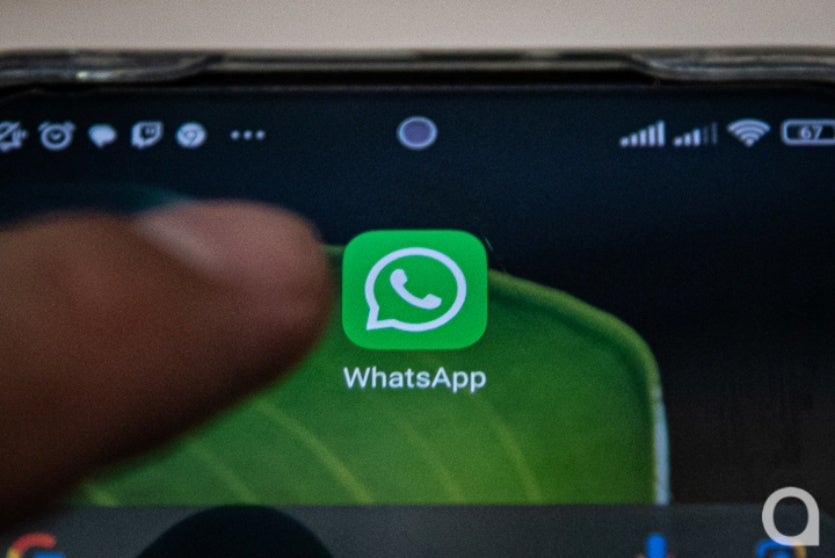Mão clicando no botão do WhatsApp em um smartphone.