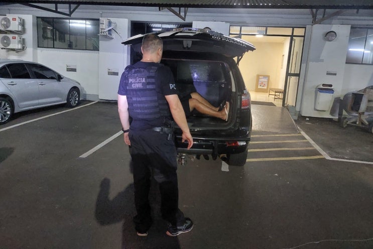 Policial conduzindo um preso ao interior de uma viatura da PCPR.