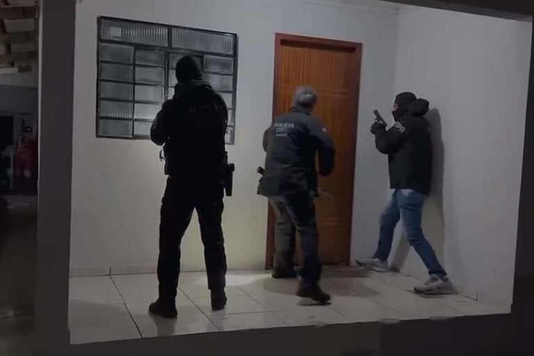 Policiais entrando em uma residência durante a Operação Teia Logística.