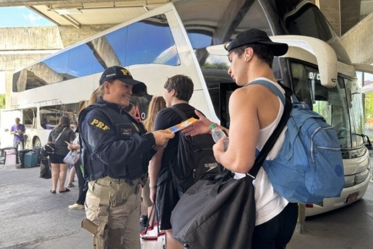 Policial rodoviário federal fiscalizando e orientando passageiros de um ônibus.