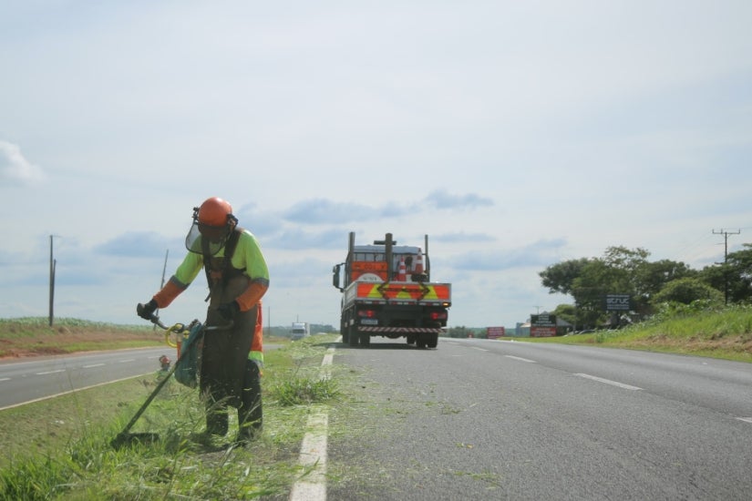 Trabalhador da EPR realizando roçada em grama dde canteiro central de rodovia.