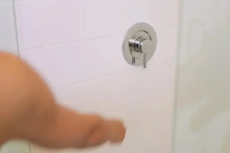 Foto de um braço ligando um chuveiro de banheiro.