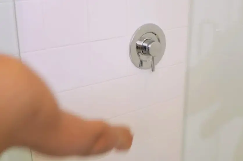 Foto de um braço ligando um chuveiro de banheiro.