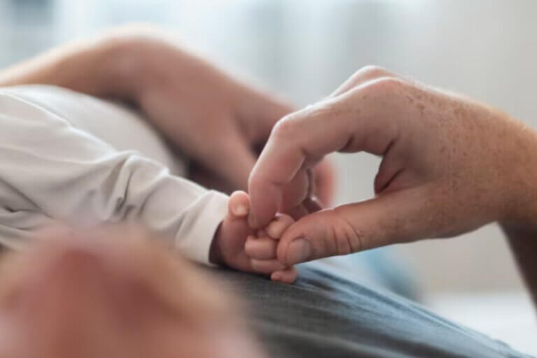 Mão adulta segurando a mãozinha de um bebê.