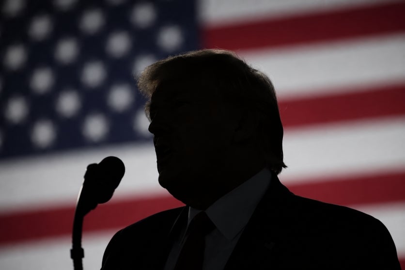 Donald Trump discursando. Ao fundo uma bandeira americana.