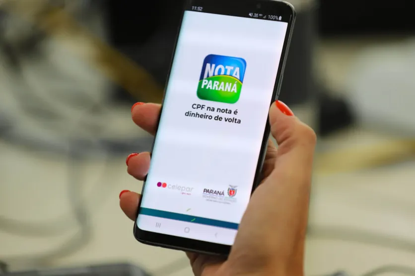 Mão segurando celular com menu do Nota Paraná.