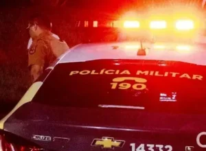 Policial militar ao lado de viatura da PM.