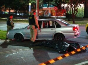 PM no local do homicídio ocorrido em Umuarama. Há o corpo coberto por uma lona no chão.