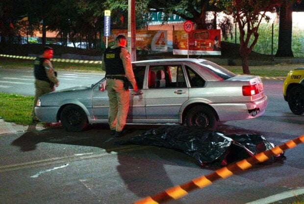 PM no local do homicídio ocorrido em Umuarama. Há o corpo coberto por uma lona no chão.