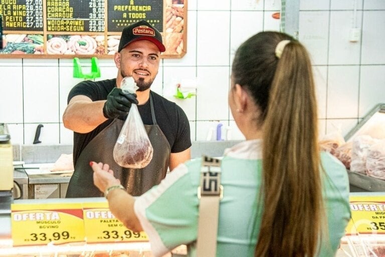 Açougueiro entregando corte para cliente no Supermercado Tuka.