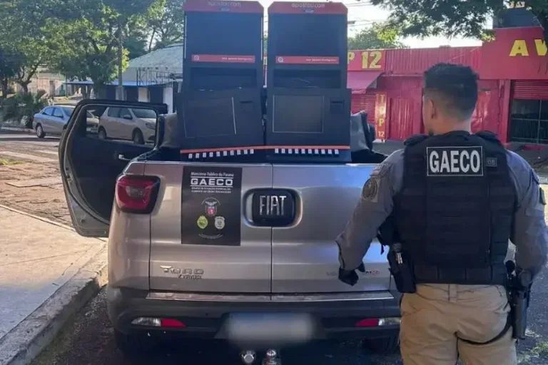 Agente do Gaeco ao lado de máquinas caça-níqueis apreendidas na Operação Alcova.