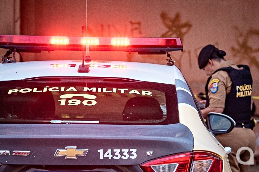 Policial militar ao lado de viatura da PM.