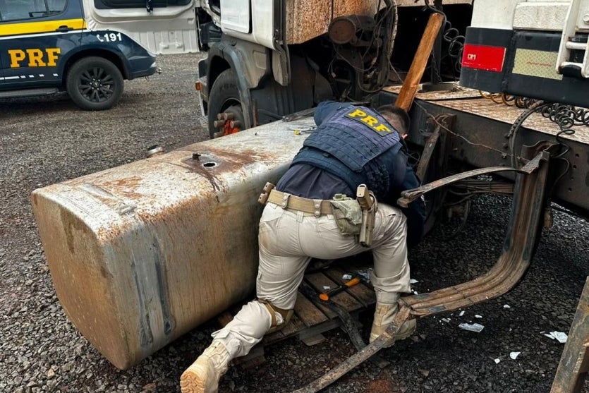 Policial conferindo tanque de carreta com cocaína.