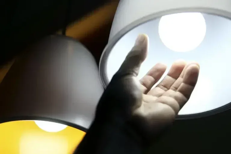 Mão após rosquear uma lâmpada acesa em um abajour.