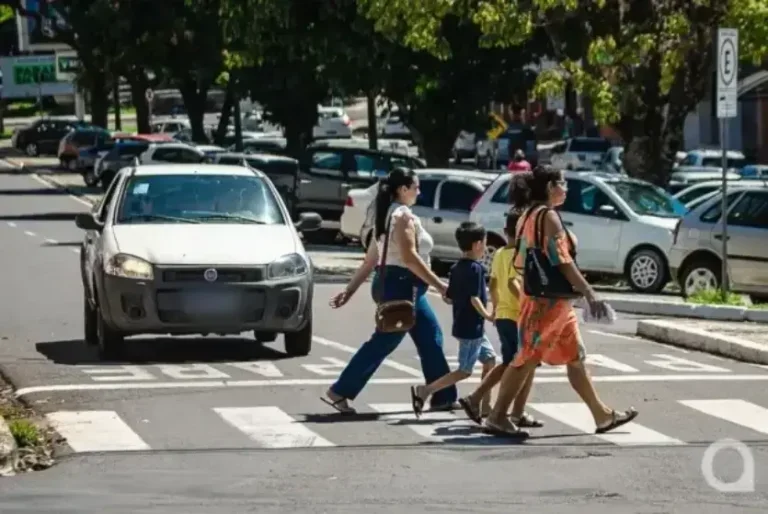 Pessoas caminhando pela faixa de pedestres enquanto carro aguarda.