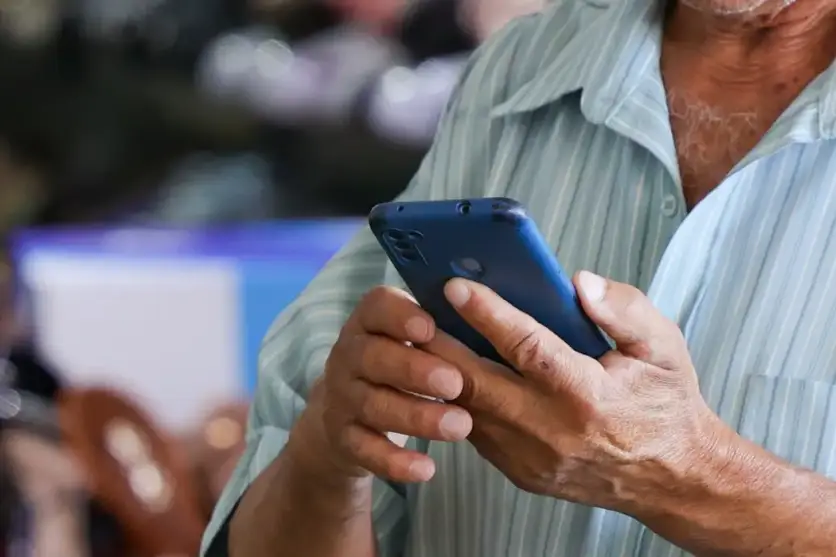 Idoso observando a tela de um celular enquanto usa o aparelho.