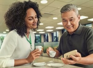 duas pessoas olhando o celular, tomando café e conversando